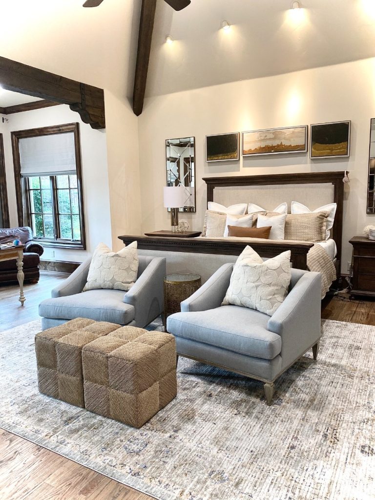 Elegant bedroom seating area with gray chairs and woven ottomans.