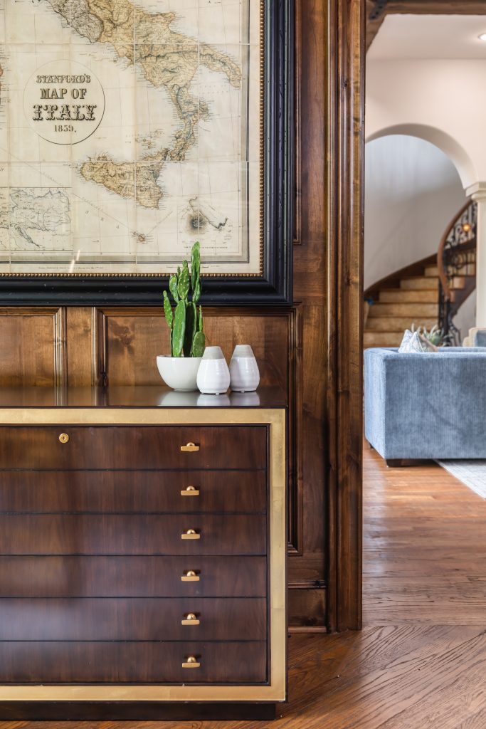 Antique map of Italy above a dark wood dresser with gold accents.
